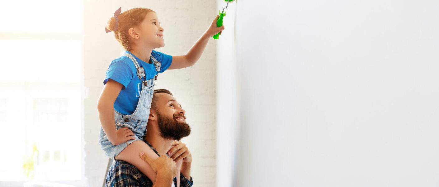 Vater trägt Tochter auf den Schultern und beide streichen eine Wand mit Farbe